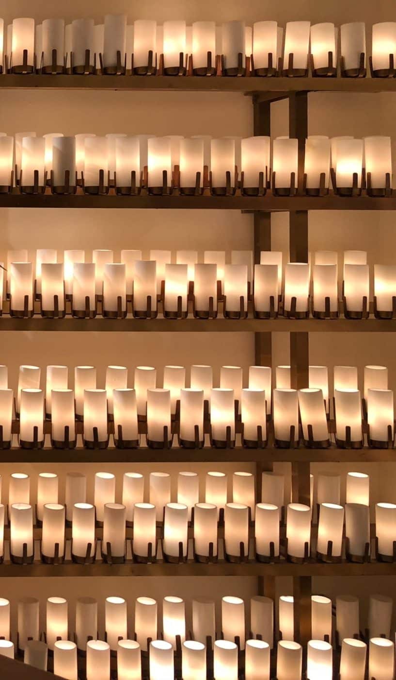 Rows of lit candles on shelves in a room at the National Shrine of St. Jude, emitting a warm glow.